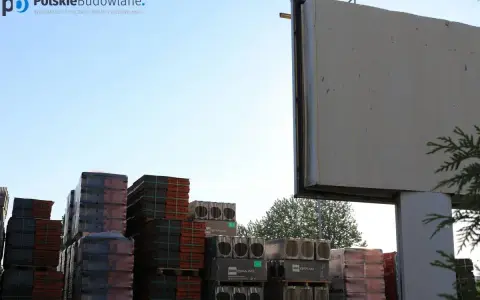 Stosy dachówek i materiałów budowlanych pod pustym billboardem. Reklama na budynku inaczej, czekająca na nowe hasło.