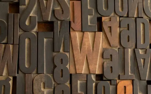 Drewniane czcionki, w tym litery z polskimi znakami, tworzą teksturę przypominającą klasyczny druk. Widać literę "W" w stylu Helvetica.