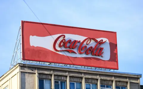 Duży baner logo Coca-Cola na dachu budynku, z charakterystyczną białą butelką i czerwonym napisem.