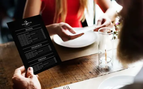 Mężczyzna trzyma czarne menu restauracji "The Dark Bear". Co to jest laminat? To trwałe menu, idealne do restauracji.