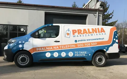 Biało-niebieski van z pomarańczowymi elementami to reklama tranzytowa dla pralni. Na boku widnieje napis "PRALNIA WARSZOWIANKA" i numer telefonu.