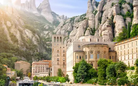 Klasztor Montserrat wznosi się wśród skalistych szczytów, z budynkami o architekturze przypominającej czcionkę Montserrat.